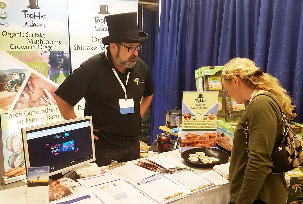 man in a top hat talking to a woman at a trade show about top hat mushrooms (Shiitake Mushrooms)
